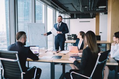 Resmi giysiler içinde kendine güvenen bir ofis çalışanı modern konferans odasında oturan ve dizüstü bilgisayarlar üzerinde çalışan yöneticilerin düzenini gösteriyor.