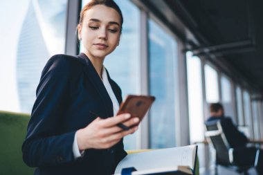 Ofis odasında koçun yanında otururken modern akıllı telefonu dikkatle kullanan resmi kıyafetli güzel bir bayan çalışana odaklanmış.