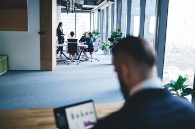 Bir grup çalışanın isimsiz yöneticinin çalışma odasının yanındaki masada otururken iletişim kurması ve iş projelerini tartışması