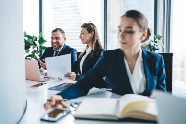 Bilgileri kontrol eden ve yeni proje üzerinde çalışan bir grup iş adamı hafif ofiste oturmuş, asistanlarıyla birlikte cep telefonlarını inceliyor. 