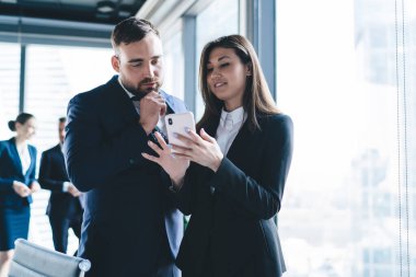 Takım elbiseli mutlu bir kadın, şehir konferans odasının penceresinin yanında resmi giyinmiş, akıllı telefon kullanıyor.