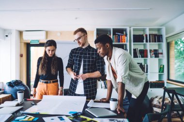 Tasarım projesinde işbirliği yapan çok kültürlü erkek ve kadın meslektaşlar plan çizimlerinde yaratıcılıkla beyin fırtınası yapıyorlar, milenyumlar birlikte çalışma alanında fikir alışverişinde bulunuyorlar.
