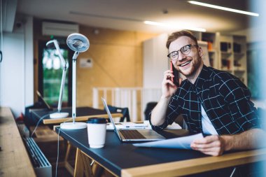 4G internete bağlı arkadaş canlısı iş arkadaşıyla mobil iletişimde gülen neşeli serbest yazar, görüş koruması için gözlüklü dişlek erkek blogcu cep telefonu sohbetinin keyfini çıkarıyor