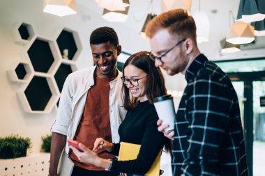 Neşeli çeşitli öğrenciler üniversitenin kamu sayfasından internet bilgilerini tartışıyorlar. İçeride duruyorlar ve konuşuyorlar. Z jenerasyonu modern cep telefonu cihazından mesaj okuyor ve gülümsüyor.