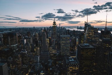 Manhattan 'ın çeşitli yüksek binalarının ve gökdelenlerinin gökdelenlerinin gökdelenleri New York şehrinde akşam gökyüzü ve bulutların arka planında yer alıyor.