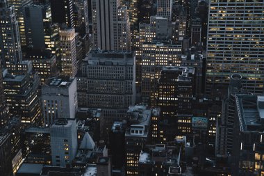 Manhattan 'ın çeşitli yüksek binalarının ve gökdelenlerinin gökdelenlerinin gökyüzü manzarası. Akşam saatlerinde New York' ta ışıklı pencereleri olan.