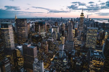 Manhattan bölgesinin parlayan yüksek binalarının gökyüzü arka planında New York şehrinin ışıklandırılmış pencereleri olan hava manzarası.