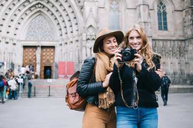 Barcelona 'nın ünlü tarihi katedralinin yanında durup kamerayla gülümseyen ve fotoğraf çeken mutlu bir çift kadın gezgin.