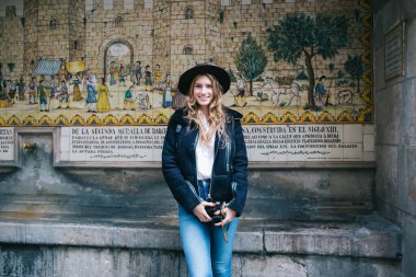 Neşeli, genç, çekici, sarışın, şapkalı, gülümseyen ve elinde fotoğraf makinesi olan gezgin bir kadın.