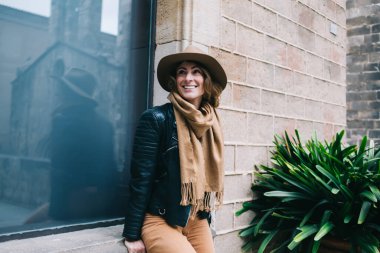 Dişi gibi gülümseyen, deve rengi şapkalı ve siyah ceketli açık hava penceresinde oturan neşeli sarışın genç bir kadın.