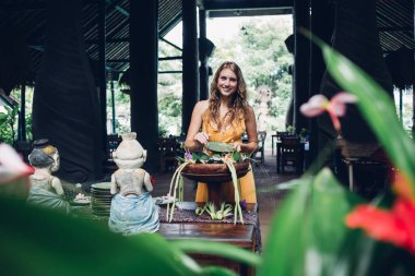 Masanın önünde duran güzel, uzun saçlı kadın tabaklar ve geleneksel heykellerle çay saatinde büyük ahşap tepsiden atıştırmalıklar ve şekerlemeler alıyor.