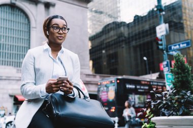 İyi ki şık giyinmiş ve gözlüklü Afro-Amerikan bir kadın akıllı telefon kullanıyor ve şehir caddesinde oturup telefonlara cevap verirken yüzünü çeviriyor.
