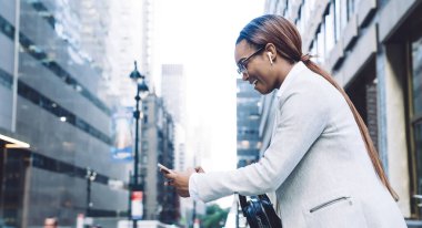 Düşük açılı Afrika kökenli, heyecanlı, ağzı açık, ekrana odaklanan ve yüksek binalara karşı caddede duran akıllı telefonla iletişim kuran düşünceli, Afro-Amerikan kadınının bakış açısı.