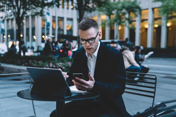 Vážný Mladý Formální Obchodník Brýlemi Obleky Procházející Mobilní Zatímco Sedí — Stock fotografie