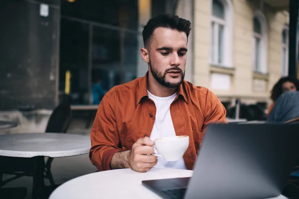 Sério Jovem Confiante Camisa Laranja Assistindo Laptop Enquanto Faz Trabalho — Fotografia de Stock