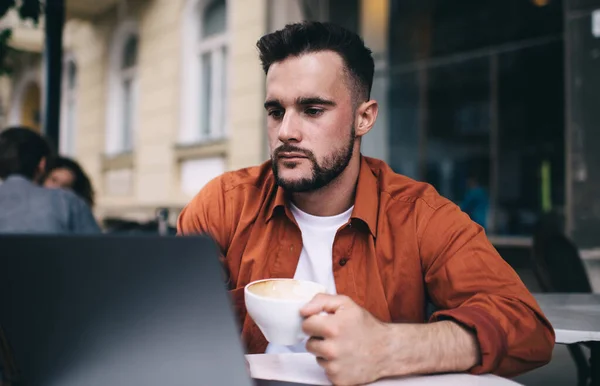 Tânăr Arătos Cămașă Portocalie Care Navighează Laptop Bea Cafea Vara — Fotografie, imagine de stoc