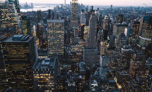 Aerial view of skyscrapers and towers in midtown skyline of Manhattan with evening sunset sky. Scenery cityscape of financial district with famous New York Landmark, illuminated Empire State Building