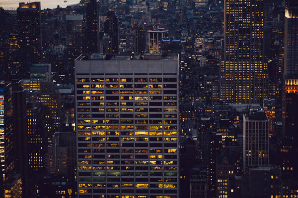 Aerial view of various high Manhattan skyscrapers buildings with lighted windows located in New York city at evening time. Night life of metropolis, offices and real estate. Downtown structures