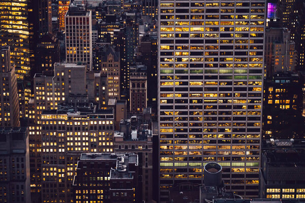 Aerial view of various high Manhattan skyscrapers buildings with lighted windows located in New York city at evening time. Night life of metropolis, offices and real estate. Downtown structures