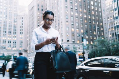 Gözlüklü ve resmi kıyafetli şık bir ofis çalışanı, şehir caddesinde cevap vermek için cep telefonunu kullanan meslektaşından mesaj alıyor.
