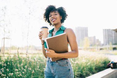 Güneşli bir günde kahve içmek için kıvırcık saçlı, esmer hippi kızın yarım boy portresi. Çekici Afrikalı Amerikalı kadın moladan ve boş zamanlardan zevk alıyor.