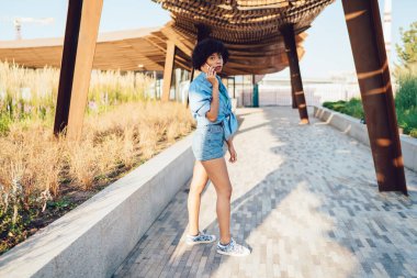 Çekici moda, koyu tenli hippi kız cep telefonuyla konuşuyor, şehir parkında yürüyor, genç Afrikalı Amerikalı kadın yazın güneşli da 'yı ziyaret ederken arama yapıyor.