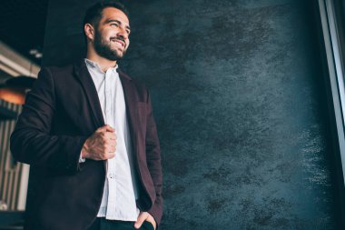 Resmi moda kıyafetleri içinde mutlu beyaz erkek girişimci. Kapalı alanda başarılı bir kariyerden memnun, duvarın arkasında gülümseyen bir kafenin varlıklı genç sahibi.