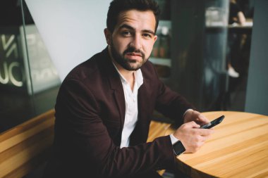 Resmi kıyafetli, elinde cep telefonu olan, modern aletler kullanarak mesaj gönderen yakışıklı beyaz bir adamın portresi. Bin yıllık ciddi özgüveni olan bir adam, akıllı fondaki uygulamayla posta gönderen kameraya bakıyor.