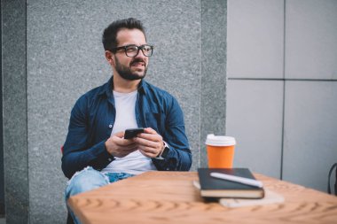 Kafe 'de kahve molası veren yakışıklı beyaz tenli hippi adam akıllı telefonuyla blog' a içerik gönderiyor. Milenyum boyunca cep telefonundan yapılan kontrol uyarıları.