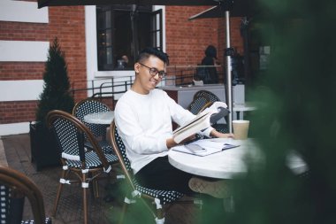Asyalı pozitif hevesli genç erkek büyüleyici bir kitap okurken ve şehir kafesinin dışındaki masada otururken ilham alıyor.