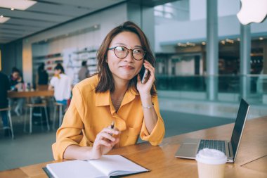 Telefonla konuşan ve Hong Kong 'da açık büfede dizüstü bilgisayarla ve kahveyle notlar alan Asyalı bir kadın işçi.