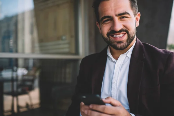 Half length portrait of cheerful caucasian bearded businessman using mobile phone browsing, happy male entrepreneur satisfied with good 4G connection sending mail on smartphone sitting outdoors
