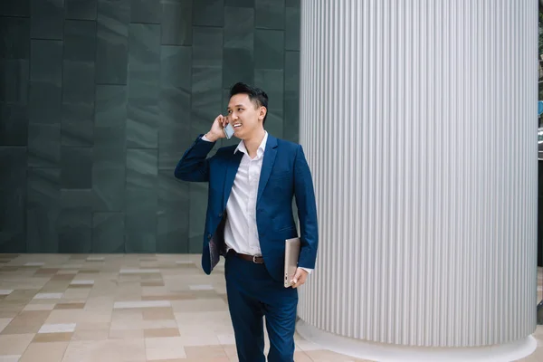 Sorrindo Bonito Homem Asiático Terno Elegante Segurando Laptop Enquanto Chamando — Fotografia de Stock