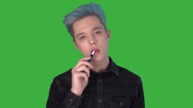 Elektronik sigara içen genç adam yeşil ekran kameraya bakıyor.