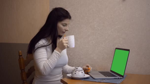 Junge Frau arbeitet Laptop mit grünem Bildschirm am Küchencomputer und trinkt Kaffee — Stockvideo