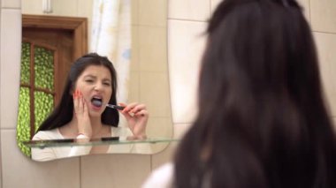 Genç kadın dişlerini fırçalarken güçlü diş ağrısı aynada yanağına dokunuyor.