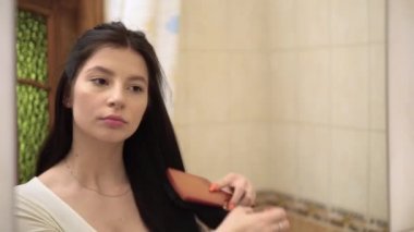 Yoğunlaşmış uzun saçlı kız aynada yansıyor saçlarını sabah tarıyor