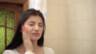 Aynadaki genç kadın, dişlerini fırçalarken güçlü bir diş ağrısı hisseder.