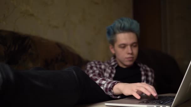 Молодой человек болтает на ноутбуке, печатает клавиатуру на диване дома — стоковое видео