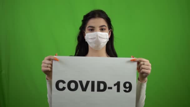 Mädchen in medizinischer Maske mit einem COVID-19-Schild auf grünem Bildschirm. Coronavirus singt. — Stockvideo