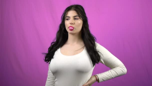 Дівчина дме жувальна гумка на фіолетовому фоні, жувальна гумка сексуальна брюнетка повільно — стокове відео