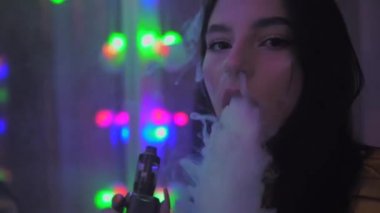 Esmer kız sigara içiyor, sigara içiyor, elektronik sigara içiyor, aynayı kapatıyor.