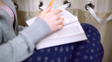 Genç bir kadın kitap okuyor, sayfaları çeviriyor, evde dinleniyor, rahat bir oturma odası, dinleniyor.