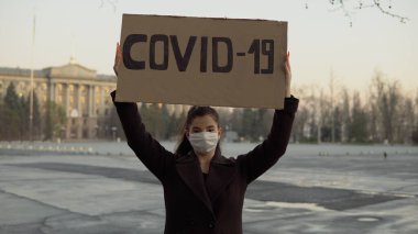 Kızın elinde COVID-19 işareti var. Boş bir bölgede, karantina, koronavirüs, maske.