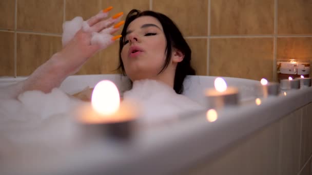 Köpük banyosunda rahatlatıcı genç bir kadın. Banyoda mumlarla romantik bir atmosfer. — Stok video