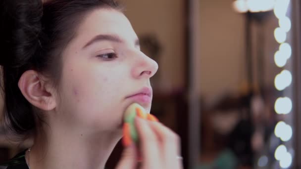 Chica joven mirando el espejo de gran visage poner maquillaje, base de mezcla, corrector — Vídeo de stock