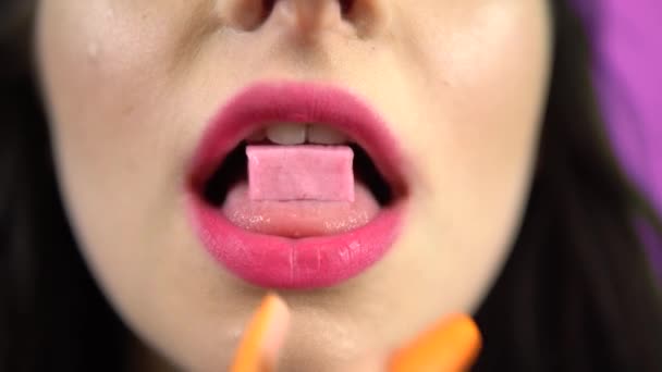 Молода жінка кладе цукерки з жувальної гумки в рот, крупним планом портрет, рожеві губи — стокове відео