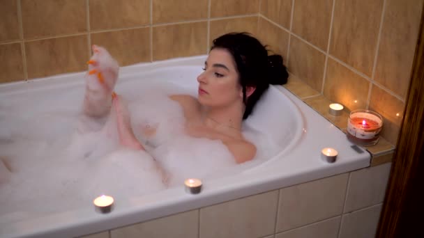 Young brunette woman relaxing on bubble bath with candles self-care evening — Stock Video