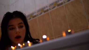 Banyodaki ıslak kız mumları üflüyor, romantik bir ortam.