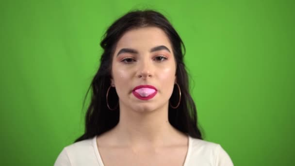 Young sexy smiling girl blowing bubble gum on green screen — Stock Video